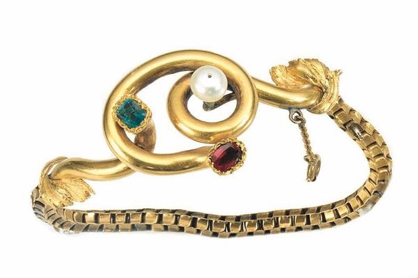 Bracciale, fine sec. XIX, in oro giallo, rubino, smeraldo e perle lavorato a maglia tubolare, al centro elemento rigido a volute contrapposte decorate da piccole foglie cesellate, pietre di colore e perla, g 26