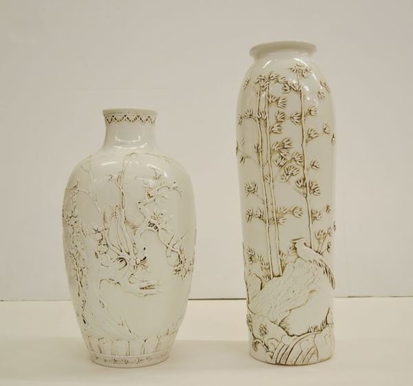 Due Vasi Cina sec. XX, in porcellana bianca uno dalla forma ad anfora decorato con grande albero a rilievo, l'altro di forma cilindrica decorato con fenice su una roccia in un bosco di bamboo, alt. cm 34; alt. cm 44 (2)