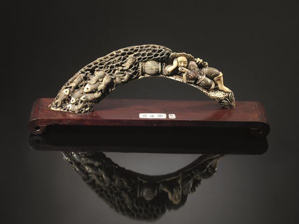 Zanna Cina sec. XIX - XX, in osso proabilmente di facocero, finemente       intagliata con pescatore sdraiato attorniato da rete con pesci, lung. cm cm 27x13, su base in legno alt. cm 2,5, restauri,                              lievi mancanze
