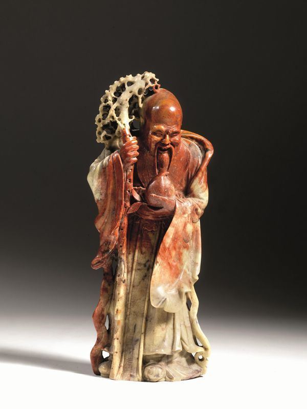 Scultura Cina, sec. XIX-XX, in pietra saponaria raffigurante Shoulao, dio taoista della longevitÃ  dal cranio pronunciato e appoggiato al lungo bastone, pesca nella mano destra, la pietra saponaria caratterizzata da venature color ruggine, alt. cm 31