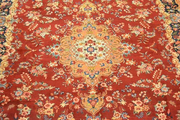 Tappeto persiano KIRMAN, firmato, di vecchia manifattura, fondo rosso, campo a motivo floreale multicolore, medaglione centrale, bordura blu, rosso mattone e celeste, cm 375x295