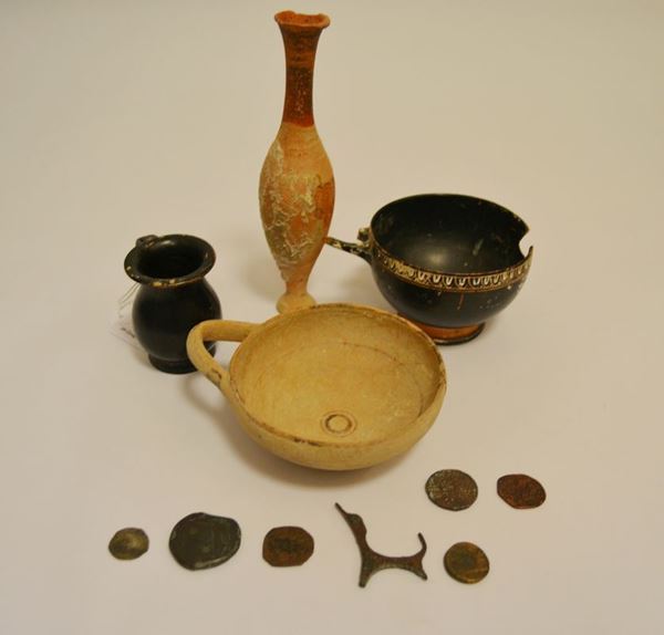 Skyphos nello stile di Gnathia, olpe miniaturistica a vernice nera, coppetta daunia monoansata ed un unguentario fusiforme   Materia e tecnica: argilla figulina rosata, vernice nera lucente, suddipinture a vernice bianca, modellati a tornio veloce  Dimensioni: alt. da cm 18 a cm 4,8   Datazione: IV-I sec. a.C.   Sei monete in bronzo varie epoche e un frammento in bronzo