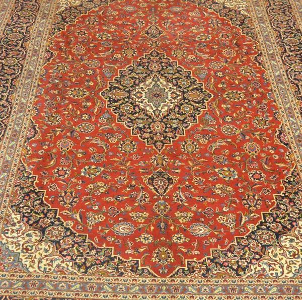 Tappeto persiano KEISHAN firmato, in lana kork extra fine, colori vegetali naturali, campo a motivo floreale, fondo rosso con medaglione centrale e bordura blu, azzurro e beige, cantonali azzurro, cm 405x290