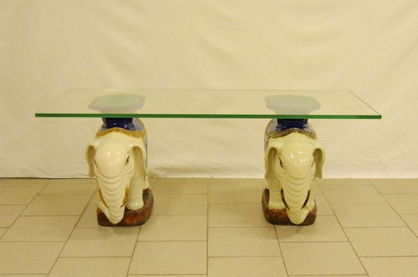 Tavolino, sec. XX, piano in vetro su due basi in maiolica a forma di elefanti, cm 137x60x55