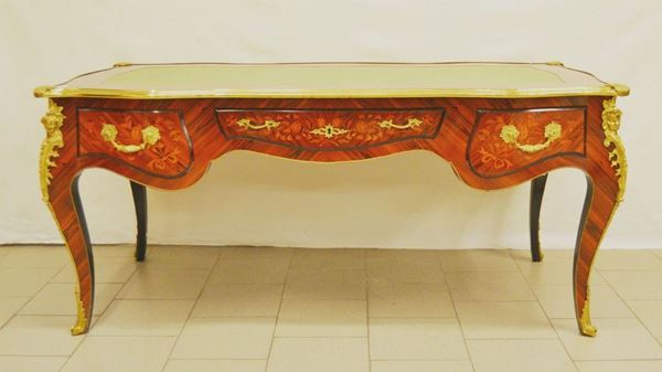 Tavolo scrivania, in stile Luigi XV, piano sagomato rivestito in pelle verde, bordi in metallo dorato, fronte mosso a tre cassetti con decori floreali, gambe a sciabola, cm 176x83x78