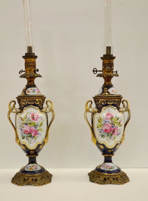 Coppia di lampade a petrolio, sec. XIX, in porcellana fondo blu con riserve decorate a scene galanti in policromia, guarnizioni in bronzo dorato, alt. cm 60 (2)