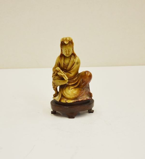 Intaglio Cina sec. XX, in pietra saponaria, raffigurante Guanyin, assisa con scroll, alt. cm 12, su base in legno