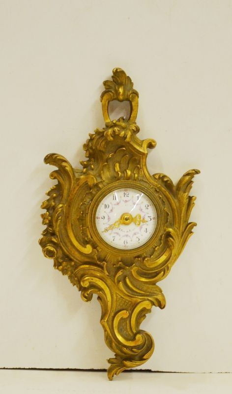 Piccolo orologio, Francia, fine sec. XIX, in metallo dorato e sbalzato a motivo rocaille, quadrante in smalto bianco con numeri arabi, alt. cm 21, meccanismo da revisionare