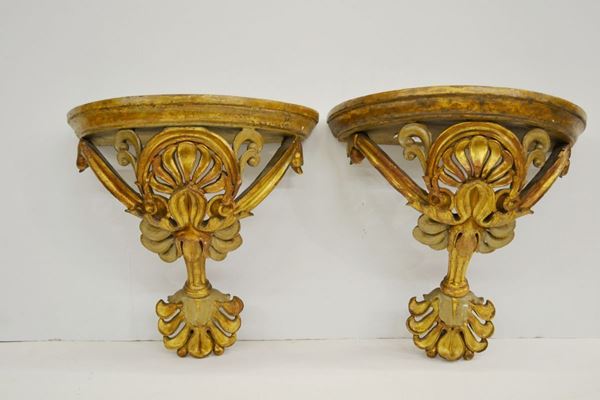 Coppia di mensoline porta oggetti, fine sec. XIX, in legno intagliato e dorato, piano semicircolare, sostegno modellato a doppia palmetta tra volute, cm 34x19x32, danni e ridorature