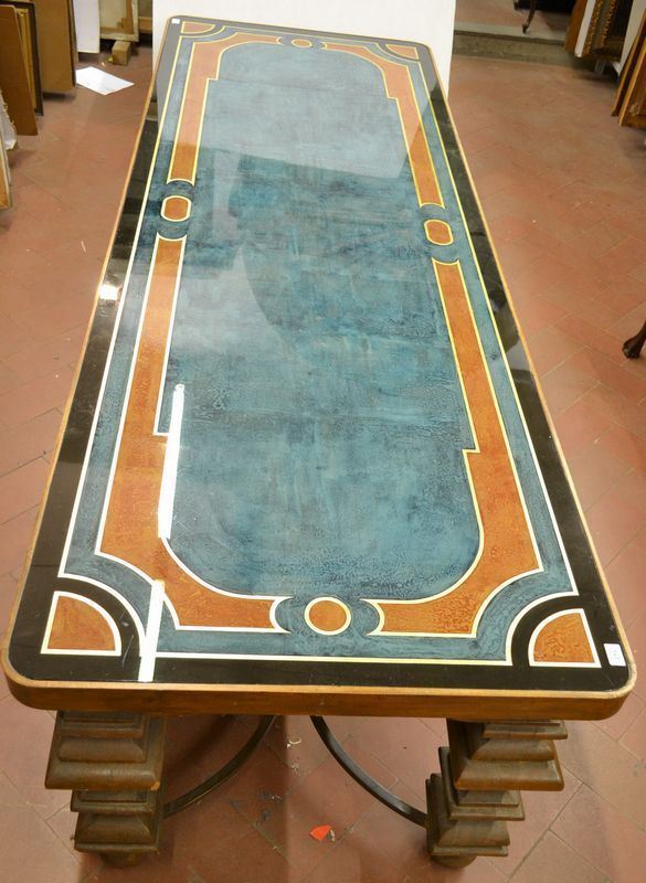 Grande tavolo da centro, in noce intagliato, piano rettangolare con angoli arrotondati dipinto a finti marmi policromi a motivi geometrici ricoperto da un piano in vetro, gambe a balaustro riunite da crociera in bronzo, cm 260x90x7
