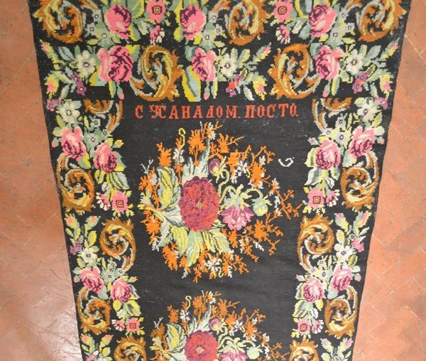  Tappeto russo,  fondo nero decorato nei toni del verde e del rosso e del rosa con fiori ed iscrizione in cirillico, cm 440x180,  consunto 