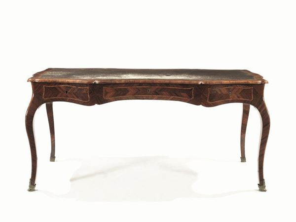  Bureau-plat, sec. XX, in stile Settecento , in bois de rose e bois de violette, piano rettangolare sagomato ricoperto in cuoio, fascia mossa con tre cassetti, alte gambe sinuose con scarpette in bronzo, cm 165x83x80                                     