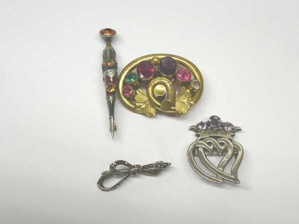 QUATTRO SPILLE IN ARGENTO, METALLO DORATO E PIETRE DI COLORE rispettivamente di forma circolare in metallo dorato con vetri colorati; di forma fiocco in argento e marcasiti; di forma allungata con pietre di colore; a doppio cuore sormontato da una corona in argento e pietre porpora, punzoni inglesi,  g 28 complessivi