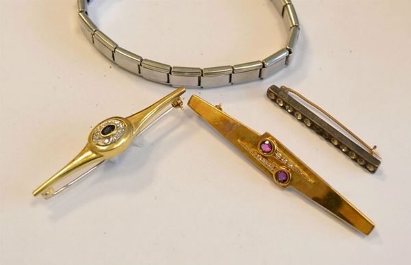   Spilla in oro giallo, zaffiro e diamanti  di forma allungata, al centro corolla decorata con zaffiro e cornice di brillanti , g 5,5   Spilla in oro giallo, rubini e diamanti  di forma stilizzata e decorata con rubini e brillanti , g 11,2  Spilla in metallo e pietre bianche   Braccialetto acciaio, lettere in oro  con scritta Marco (4) 