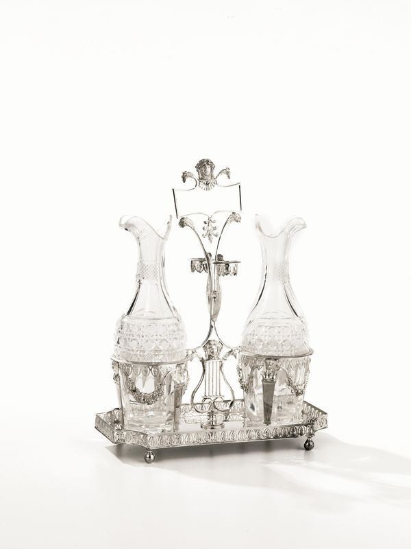   OLIERA, ITALIA, META' SECOLO XIX&nbsp; in argento, base rettangolare con bordo traforato e poggiante su quattro piedini a sfera, fusto modellato come una lira con marscheroni, presa geometrica terminante con teste di aquile, completa di ampolle, alt. cm 29,5, g 690