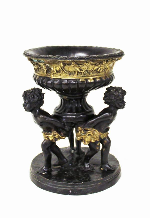 Centro tavola, sec. XX, in metallo patinato bronzo, vaso a cratere a riserva istoriata sorretto da tre putti; alt. cm 28