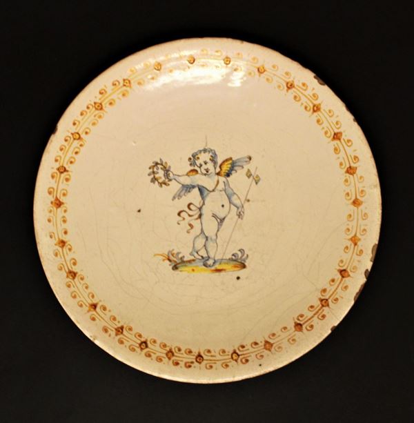 Piatto, Faenza, sec. XVII, in ceramica dipinta decorata al centro&nbsp; con putto alato con ghirlanda, diam. cm 30,5