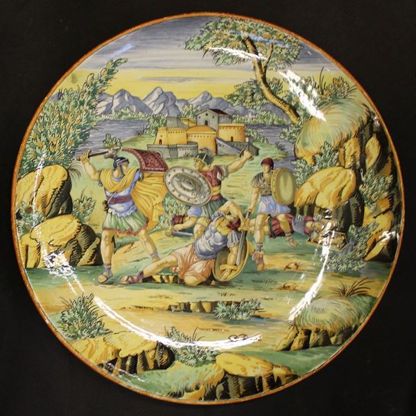 Grande piatto da parata, sec. XX, in maiolica invetriata decorata in policromia, raffigurante paesaggio con battaglia, diam. cm 52,5