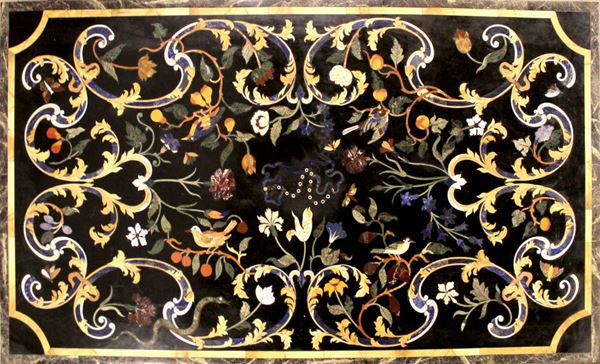 Piano di tavolo rettangolare, sec. XX, in commesso di pietre dure, fondo in marmo nero del Belgio commesso con malachite, lapislazzuli, ametista, serpentino, onice, calcedonio e marmi a formare decoro a grandi girali contrapposte fogliate e fruttate con uccelli, farfalle e serpentelli, competa il decoro al centro collana di perle, cm 93x161  - Asta GIOIELLI, ARREDI D'ANTIQUARIATO, E DIPINTI DAL XVI AL XX SECOLO - Poggio Bracciolini Casa d'Aste