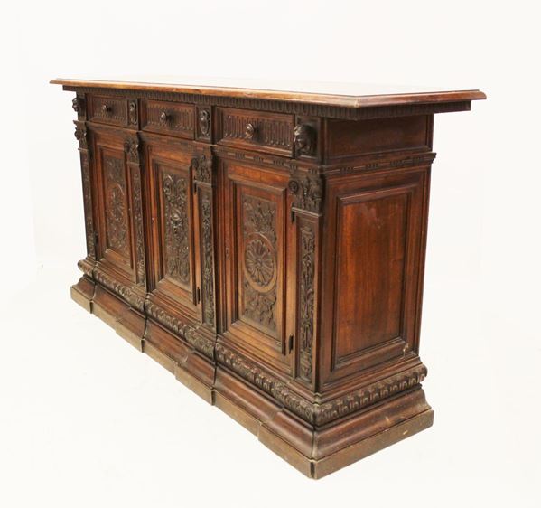 Credenza, in stile Rinascimento, in gattice, piano rettangolare a becco di civetta sotteso da motivo a dentelli incavi, fronte tripartito in tre sportelli e tre cassetti intagliati a grottesche scanditi da paraste, piede a fascia continua, cm 208x57x119