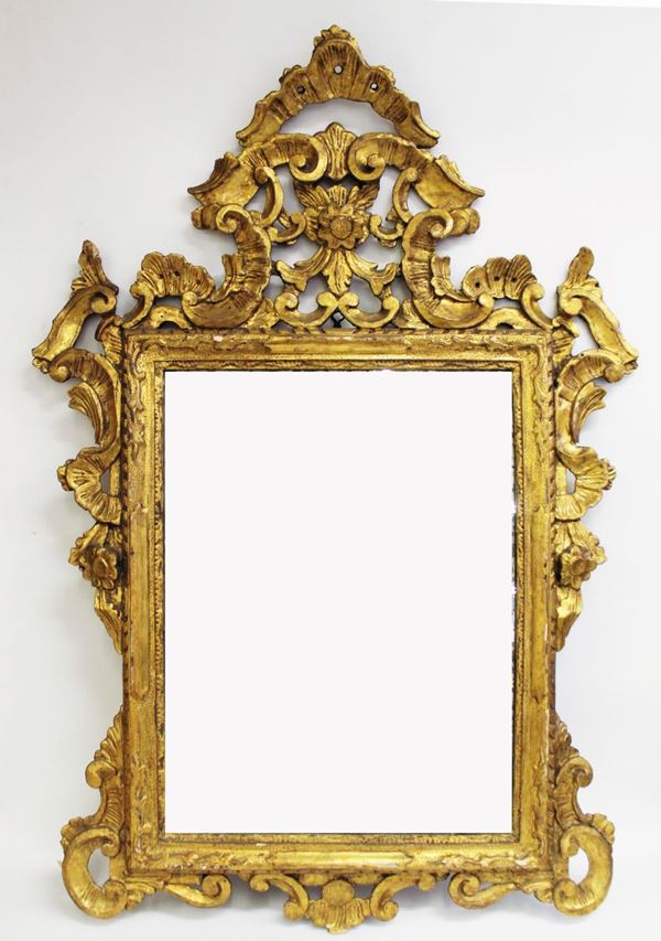 Specchiera, sec. XVIII, in legno intagliato e dorato, luce rettangolare, ampia cimasa scolpita a volute contrapposte centrata da motivo rocaille, cm 101x78, difetti
