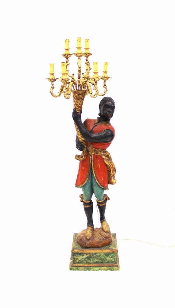 Moro reggicero, sec. XX, in legno intagliato e laccato in policromia, raffigurante moretto stante con cornucopia da cui si dipartono otto bracci a volute disposti su due ordini desinenti in punti luce, alt. cm 166