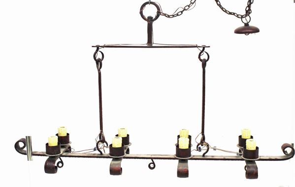 Grande lampadario, sec. XX, in ferro battuto e laccato nei toni del rosso ad otto punti luce disposti a coppie lungo due file, scartocci in vetro, cm 154x37x94