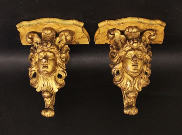 Coppia di mensoline, sec. XVIII, in legno intagliato, dorato e laccato a finto marmo, sostegni solpiti a volti coronati da rosetta, alt. cm 23