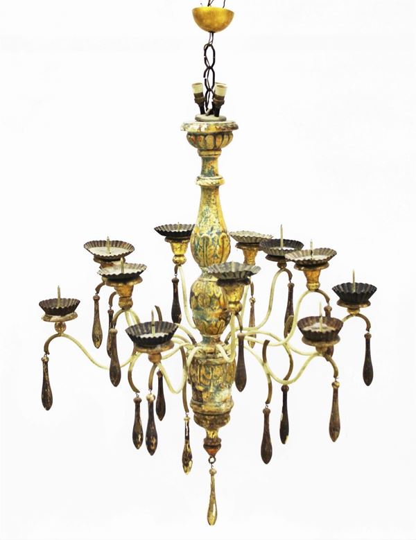Lampadario a sospensione, in stile 700, fusto centrale in legno tornito ad elementi piriformi e vasiformi intagliato a motivi fogliati e laccato in policromia,&nbsp; dodici bracci metallici a doppia voluta disposti su due ordini desinenti in bocbeches metallica, ogni braccio ingentilito da pendenti lignei a guisa di goccia, diam. cm 75, alt. cm 100, privo di impianto elettrico