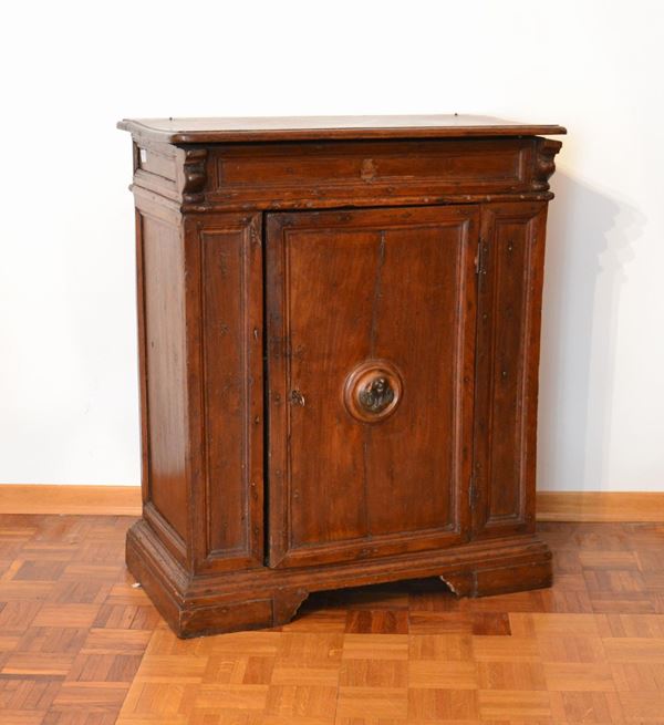 Credenzino, Emilia, sec. XVII, in noce, piano incernierato da aprirsi, uno sportello centrato da maniglia in bronzo a guisa di serafino, piedi a mensola, cm 78x45x93&nbsp;&nbsp;&nbsp;&nbsp;&nbsp;&nbsp;&nbsp;&nbsp;&nbsp;&nbsp;&nbsp;&nbsp;&nbsp;&nbsp;&nbsp;&nbsp;&nbsp;&nbsp;&nbsp;&nbsp;&nbsp;&nbsp;&nbsp;&nbsp;&nbsp;&nbsp;