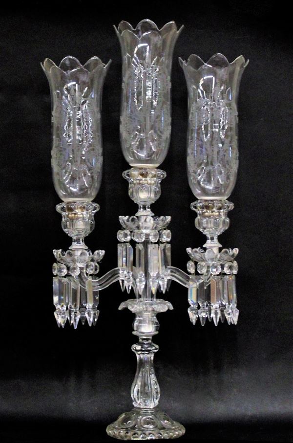 Candelabro, Francia, sec. XX, manifattura Baccarat, in cristallo incolore molato e inciso, tre bracci, impreziositi da pendenti, desinenti in campane decorate ad incisione a ramages, alt. cm 70,5