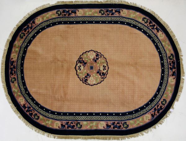 Tappeto cinese Pekino, sec. XX, di forma ovale, fondo rosa antico, fascia di bordura e medaglione centrale nei toni del blu celeste e verde, cm 255x178