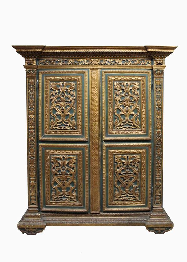 Armadio, inizi XX, in legno laccato nei toni del verde, lumeggiato in oro, fronte a due sportelli bipartiti in riserve riccamente intagliate a girali e motivi fitomorfi tra lesene decorate a grottesche, impianto decorativo che si ripresenta sui fianchi, architrave superiore scandita da mascheroni, cimasa aggettante gradinata percorsa da pi&ugrave; ordini di intagli, piedi sagomati,&nbsp; cm 197x68x235
