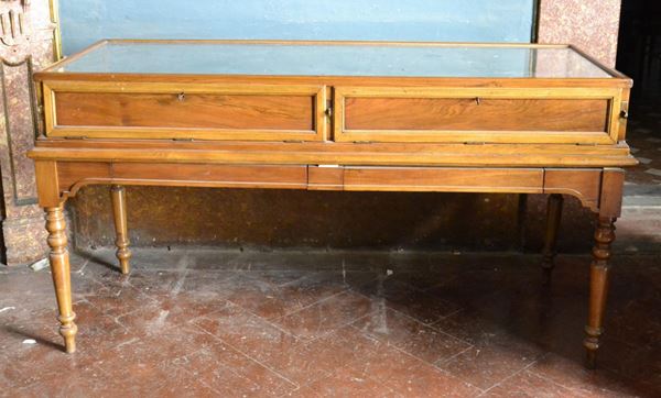 Tavolo vetrina da esposizione, inizi sec. XX, in noce, con due sportelli a ribalta, piano in vetro, gambe tornite, cm 159x66x80
