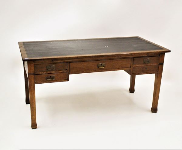 Scrivania, inizi sec. XX, in rovere, piano rettangolare con inserto in pelle nei toni del nero, tabletta estraibile sotto piano, cinque cassetti, gambe a plinto, cm 156x77x77