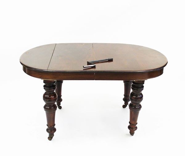 Tavolo allungabile, Inghilterra, sec. XIX, in mogano, piano ovale allungabile attraverso manovelle, quattro gambe tornite a balaustra desinenti in rotelle, cm 146,5x113x77 due allunghe da cm 34,5