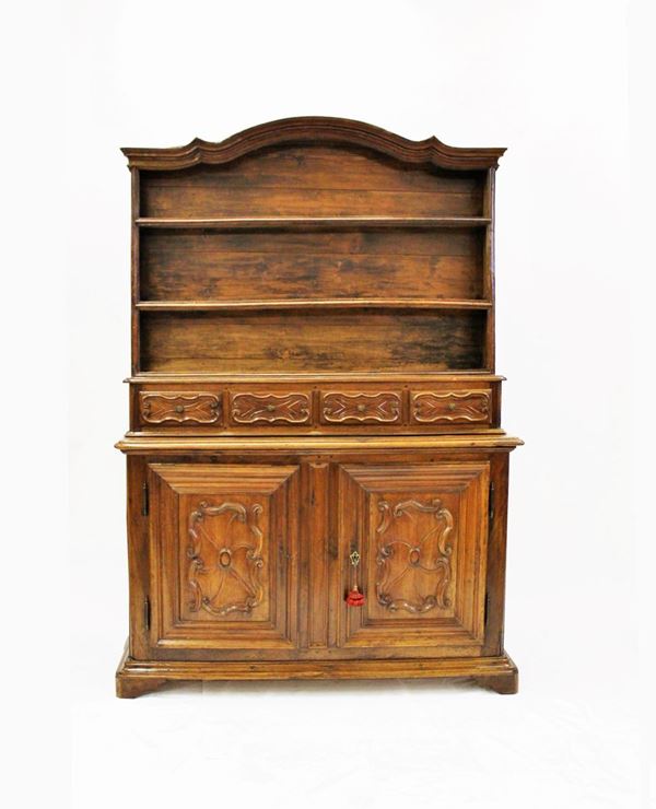 Credenza, Piemonte, sec. XIX, in noce, fronte a due sportelli a riserve bugnate a motivi curvilinei, piano rettangolare sormontato da piattaia a due mensole con fila di quattro cassetti allineati, cimasa gradinata aggettante curvilinea, cm 175x445x218