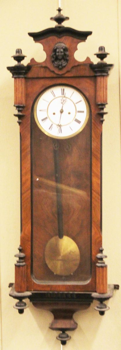 Orologio a muro, sec. XIX, cassa in legno, sportello anteriore e fianchi fetrati, cimasa modanata centrata da volto muliebre, quadrante ad indici romani, profili e nervature ebanizzati, cm 38x18x125