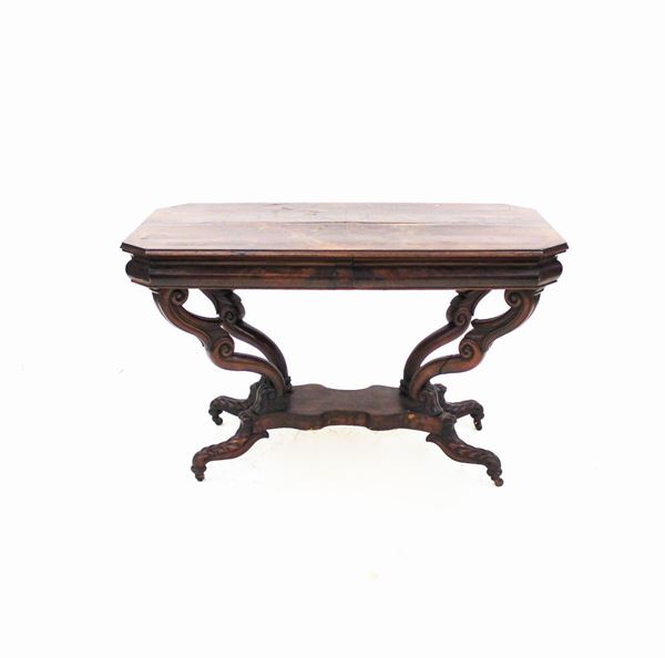 Tavolino, sec. XIX, in mogano e piuma di mogano, piano rettangolare scantonato, sotteso da coppie di cassetti allineati nella fascia, quattro sostegni fortemente sagomati e intagliati desinenti su rotelle, cm 119x62x72,5 difetti