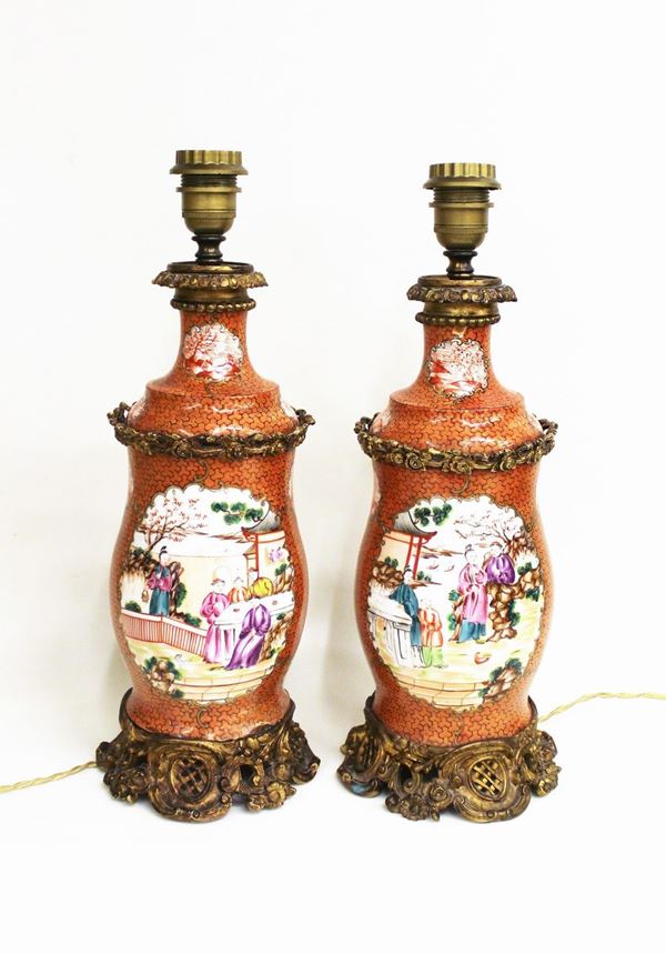 Coppia di lumi da tavolo, Cina, sec. XIX/XX, in porcellana decorata a motivi geometrizzanti a piccole riserve in monocromia nei toni del rosso e grandi riserve dipinte in policromia a personaggi, applicazioni bronzee di fattura europea, alt. cm 39, piccoli difetti