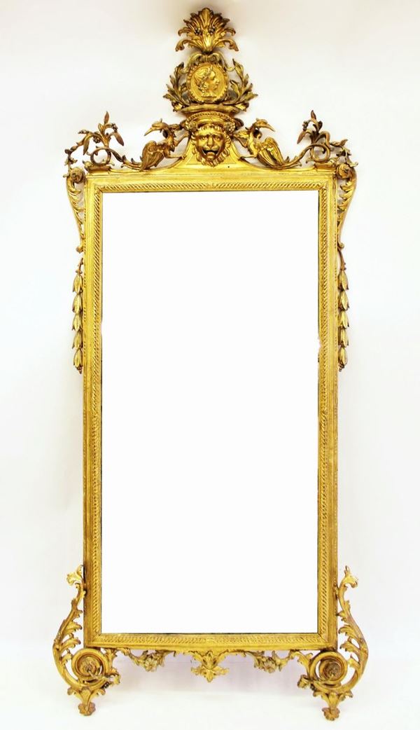Grande specchiera, Lucca, sec. XVIII, in legno intagliato e dorato, luce rettangolare percorsa da piccolo cavetto seguito da motivo a treccia e astragalo a perline e fusarole, cimasa riccamente intagliata a girali fogliate e fruttate, coppia di grifoni retrospicienti centrati da mascherone leonino sormontato da profilo di gusto classico entro clipeo coronato da palmetta fogliata rocaille, fianchi percorsi da motivi a girali e foglie lanceolate, pendaglina fogliata, piedi su ampie girali centrate da rosette, cm 240x110, usure, rotture, mancanze e cadute nella doratura, restauri, rottura dello specchio.&nbsp;&nbsp;&nbsp;&nbsp;&nbsp;&nbsp;