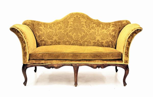 Divano a orecchioni, sec. XVIII, schienale sagomato, germbialina centinata e intagliata, rivestito in stoffa nei toni del giallo, gambe mosse, cm 175x70x98