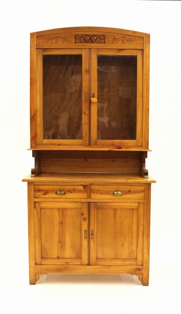 Credenza doppio corpo, sec. XX, in acero, corpo superiore a due sportelli vetrati, cimasa curvilinea scolpita a motivi fruttati e fogliati, corpo inferiore, intervallato da vano a giorno, a due cassetti allineati sottesi da coppia di sportelli, piedi a plinto, cm 120x56x236