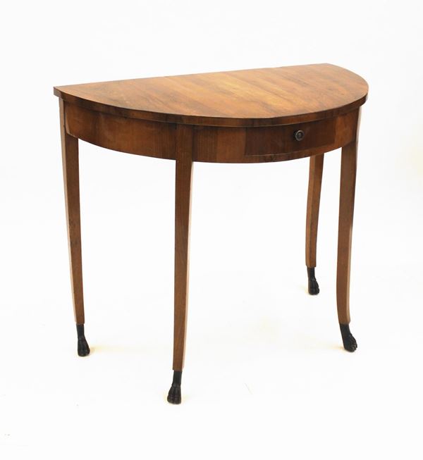 Consolle, Toscana, inizi sec. XIX, lastronata in ciliegio, piano a demilune, ampia fascia centrata da cassetto, quattro gambe leggermente mosse desinenti in piede ferino ebanizzato, cm 112x62x97