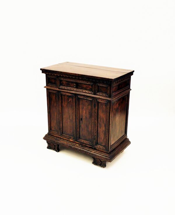Credenzino, in stile 500, in noce, piano rettangolare sotteso da motivi a dentelli incavi, fronte a cassetto e due sportelli a profili modanati, piedi intagliati, costruito con materiale antico, cm 83x45x89