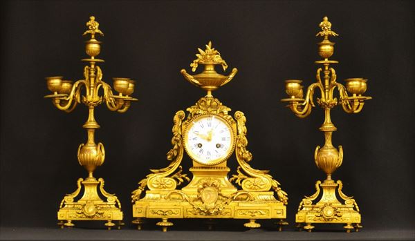 Orologio da tavolo e due candelieri, sec. XIX, in bronzo dorato e forgiato a motivi floreali, candelieri a quattro luci, orologio a mostra circolare con sovrastante vaso di fiori, alt. cm 45 e cm 40 (3)