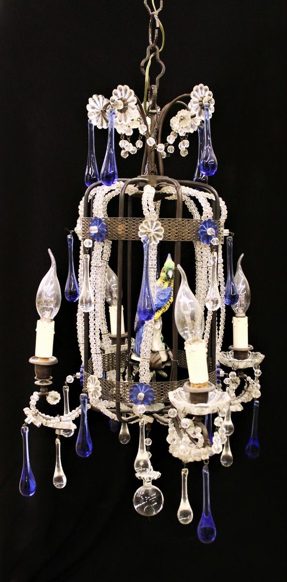 Lampadario, sec. XX, realizzato a guisa di voliera centrata da piccola scultura policroma in porcellana modellata a guisa di pappagallo, numerosi pendenti in vetro incolore e blu, alt. cm 70, diam. cm 90