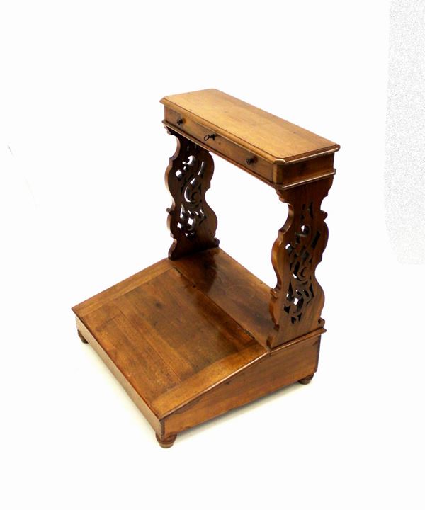 Inginocchiatoio, sec. XIX, in noce, piano rettangolare sotteso da cassetto a tutta lunghezza, montanti a giorno sagomati e traforati a volute, pedana degradante incernierata, piedi torniti, cm 69x59x85