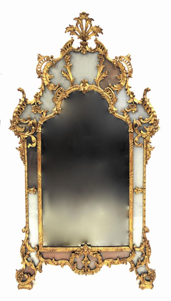 Specchiera, in stile 700, in legno intagliato e dorato, di luce di forma sagomata con ricca cimasa intagliata suddivisa in elementi specchiati, cimasa a palmetta, cm 170x100
