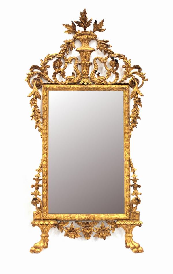 Specchiera, in stile settecento, in legno intagliato e dorato, luce rettangolare percorsa da perlinatura e fasci fogliati, ampia cimasa centrata da paniera fiorita tra tritoni e racemi, piedi ferini, cm 163,5x85